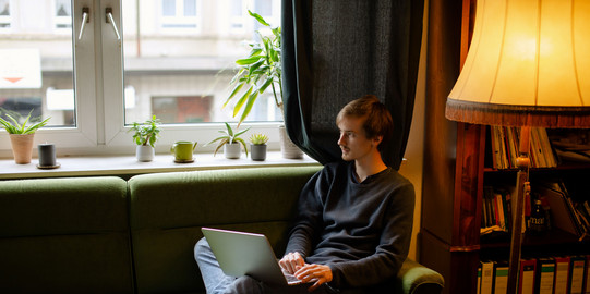 A student, sitting on the sofa, works on the laptop.